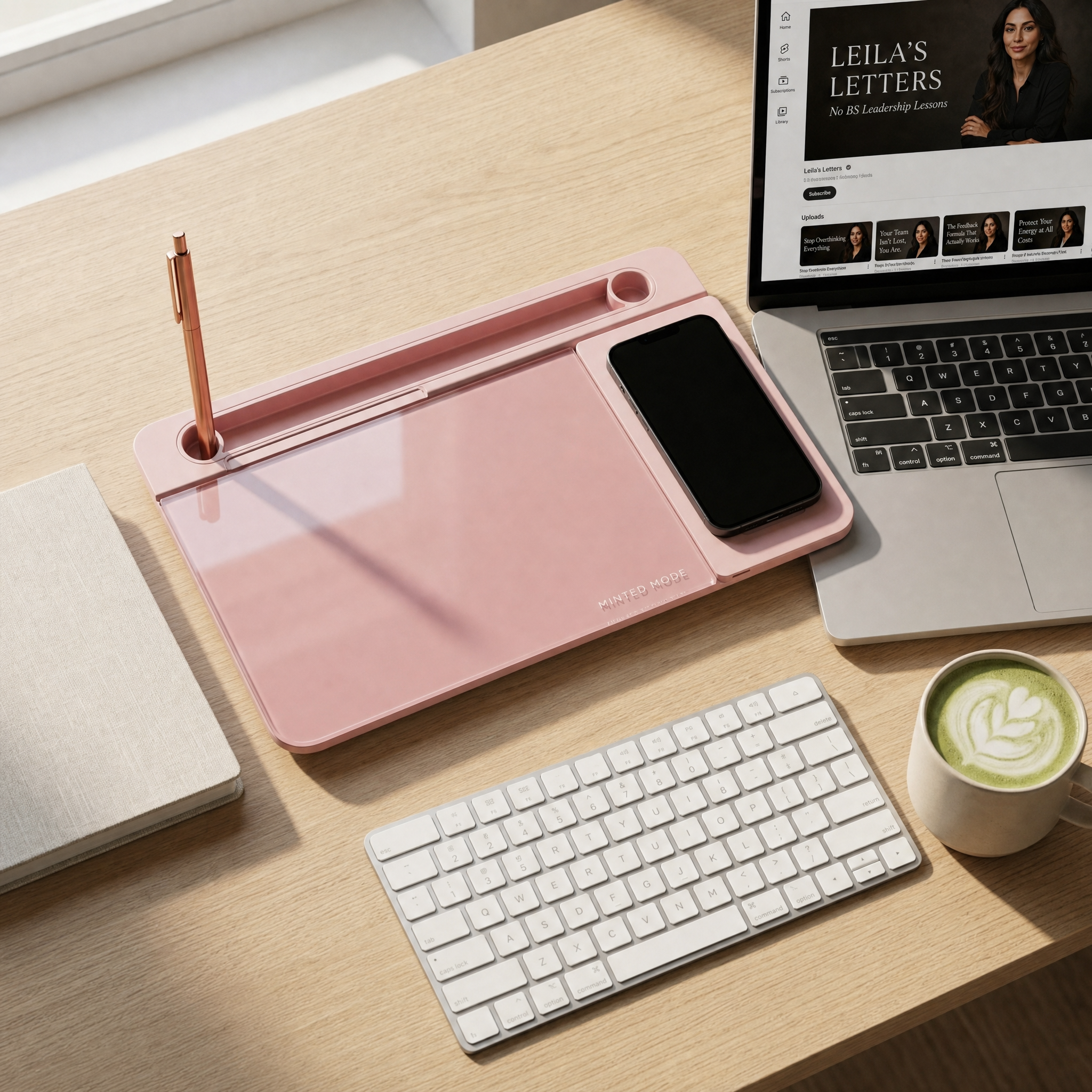 Pink desk organizer with phone, pen, and tablet on a wooden desk with laptop and coffee.