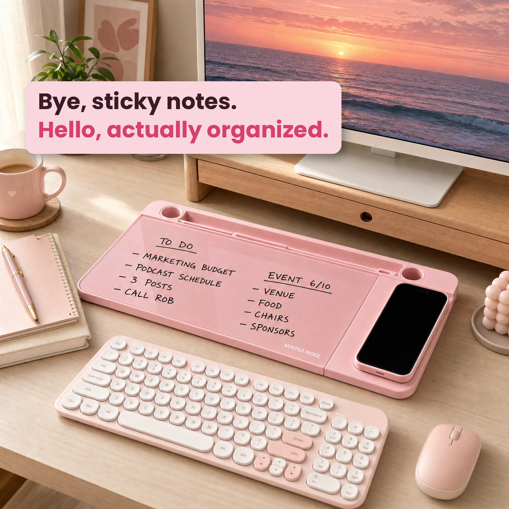 A pink magnetic desk organizer tray on a wooden desk, styled with a keyboard, mouse, mug, notebook, and a computer monitor. The tray holds a smartphone and has handwritten to-do items on its magnetic surface.
