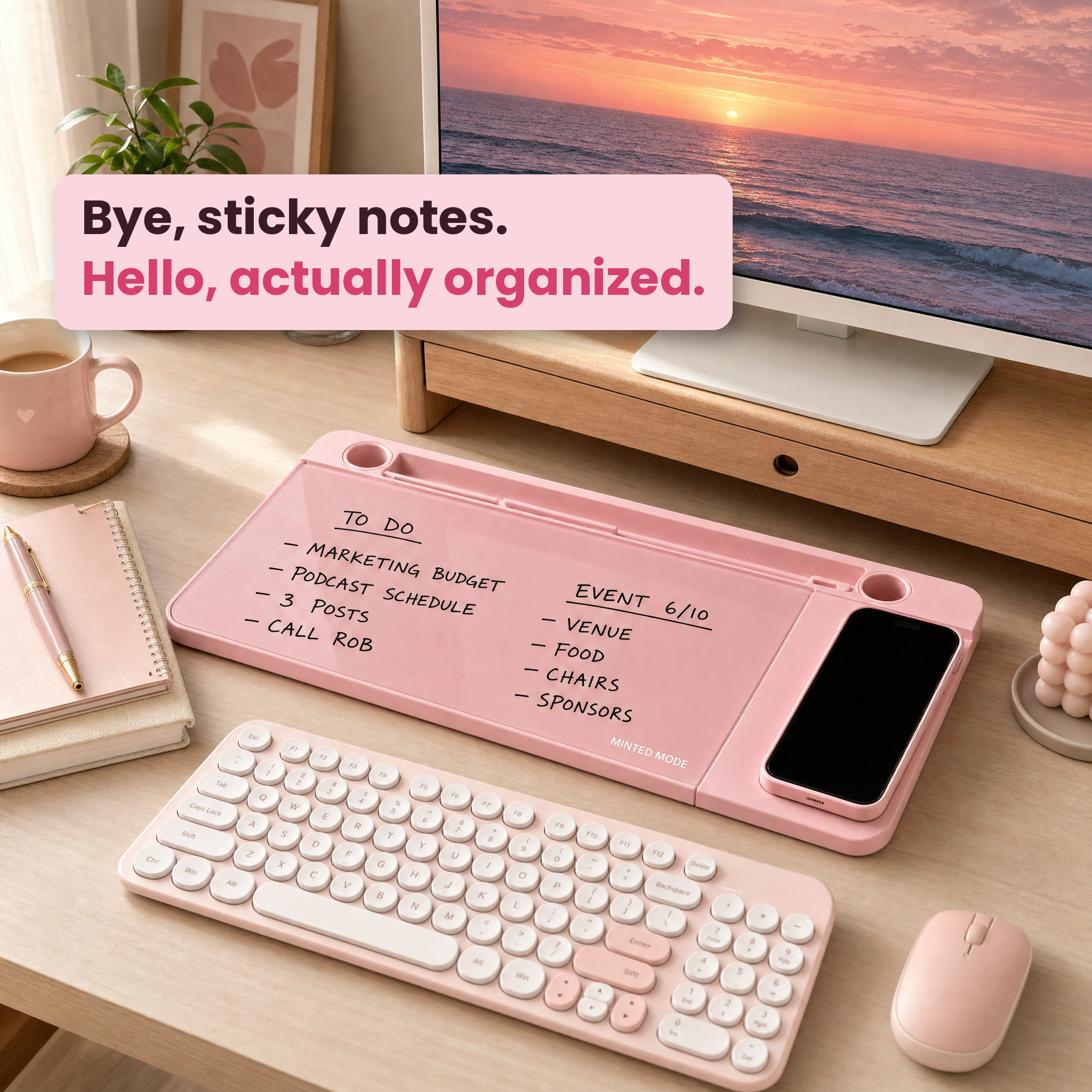 A pink magnetic desk organizer tray on a wooden desk, styled with a keyboard, mouse, mug, notebook, and a computer monitor. The tray holds a smartphone and has handwritten to-do items on its magnetic surface.